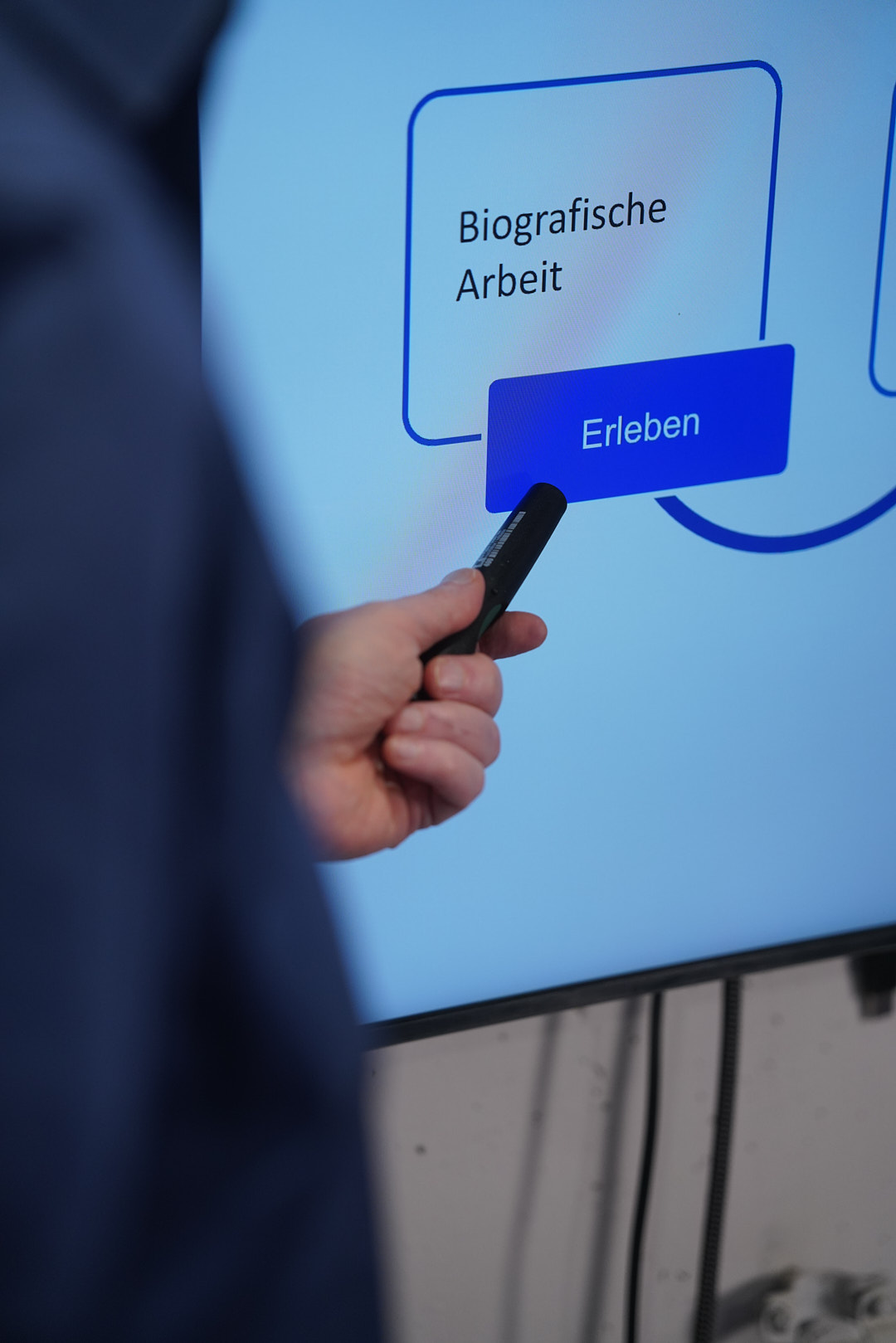 Hand mit Presenter zeigt auf einen Bildschirm mit „Biografische Arbeit – Erleben“